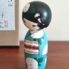 Hand-painted Kokeshi doll named Ryouhu, designed by artist Izumi, dressed in a blue kimono with morning glory flowers and a wind chime, symbolizing a cool Japanese summer breeze.