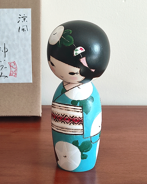 Hand-painted Kokeshi doll named Ryouhu, designed by artist Izumi, dressed in a blue kimono with morning glory flowers and a wind chime, symbolizing a cool Japanese summer breeze.