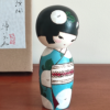 Hand-painted Kokeshi doll named Ryouhu, designed by artist Izumi, dressed in a blue kimono with morning glory flowers and a wind chime, symbolizing a cool Japanese summer breeze.