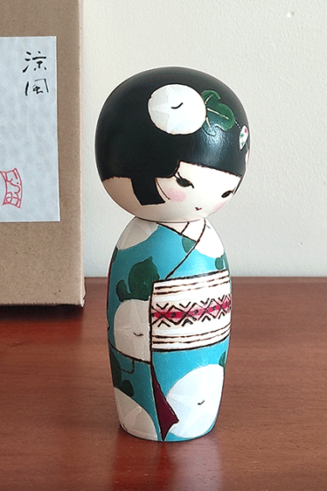 Hand-painted Kokeshi doll named Ryouhu, designed by artist Izumi, dressed in a blue kimono with morning glory flowers and a wind chime, symbolizing a cool Japanese summer breeze.
