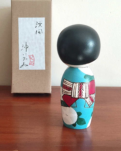 Hand-painted Kokeshi doll named Ryouhu, designed by artist Izumi, dressed in a blue kimono with morning glory flowers and a wind chime, symbolizing a cool Japanese summer breeze.