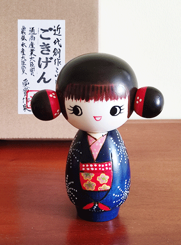 This 近代創作こけし modern creative Kokeshi doll is called 'ごきげん - Gokigen' and it was created by an award-winning artist 'ちえ Chie'. The doll's feature would be the space buns.  Her pretty Kimono has a design of Hanabi (fire works) and the obi (wide sash) has a contrast colour red. Available at j-okini.com Malta