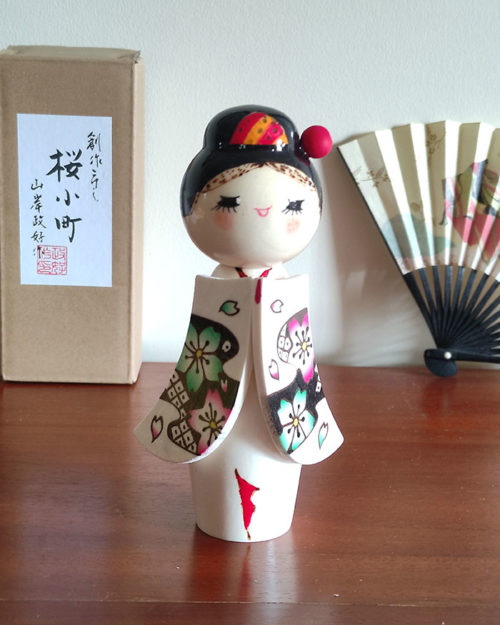 Handcrafted Japanese Kokeshi doll 'Sakura Komachi' by artist Yamagishi Masayoshi, featuring a kanzashi hair bun and a kimono with hand-painted pink and blue cherry blossoms. Available at j-okini.com in Malta