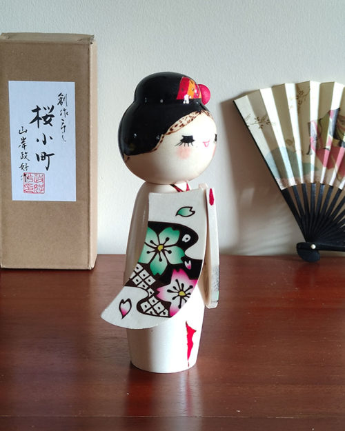 Handcrafted Japanese Kokeshi doll 'Sakura Komachi' by artist Yamagishi Masayoshi, featuring a kanzashi hair bun and a kimono with hand-painted pink and blue cherry blossoms. Available at j-okini.com in Malta
