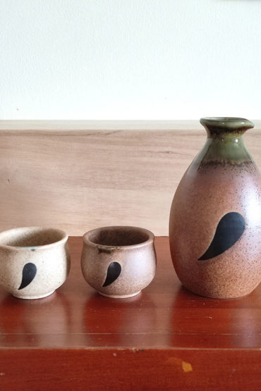 Sake set features an adorable Tanuki (raccoon dog) design, bringing a playful touch to your sake experience. The front of the sake bottle and cups showcase the face of the Tanuki, while the back reveals its tail, creating a delightful 360° design. The top portion is glazed in a rich green hue, while the unglazed bottom highlights the intricate craftsmanship of this set.. Made in Japan. Available at j-okini.com in Malta