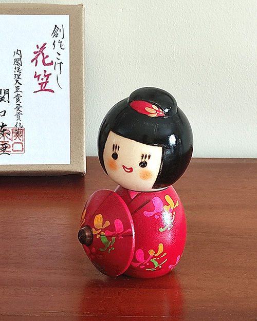 Kokeshi doll named Hanagasa holding an umbrella wearing red kimono. Made in Japan. Buy it online at j-okini.com in Malta