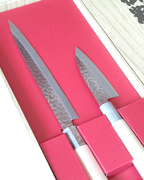 Gift masterpieces of Gifu and Seki of Japan. Yaxell is one of the major knife manufacturers in Japan since 1932, each Yaxell knife is a testament to the artistry and meticulous craftsmanship that has defined Japanese knife-making for generations, making them not just tools, but auspicious gifts that symbolize good fortune and prosperity. Made by Seki Tohei, and there are sign of 関藤平 on each knife. Blade It features a striking hammered design and provides comfortable cutting. Handle Sculpted from natural wood, designed to harmonize with your grip over time, becoming an extension of your culinary expression. This natural material not only adds to the knife's aesthetic but ensures durability and comfort with every use. This gift set includes: 1. 刺身包丁 Sashimi Bocho Overall length 330mm Blade length 205mm Weight: 79g Designed for precision, the Sashimi Bocho is the epitome of Japanese culinary artistry. Its long, slender blade is crafted to execute the most delicate and thin slices, perfect for sashimi, showcasing the knife's blend of functionality and elegance. 2.小出刃包丁 Small deba bocho Overall length 220mm Blade length 105mm Weight: 44g Specialized for handling smaller fish, this knife combines robustness and precision. Its compact design and sharp edge make it ideal for detailed work, from filleting to intricate cuts, embodying the spirit of traditional Japanese fish preparation.. Available at j-okini.com Malta