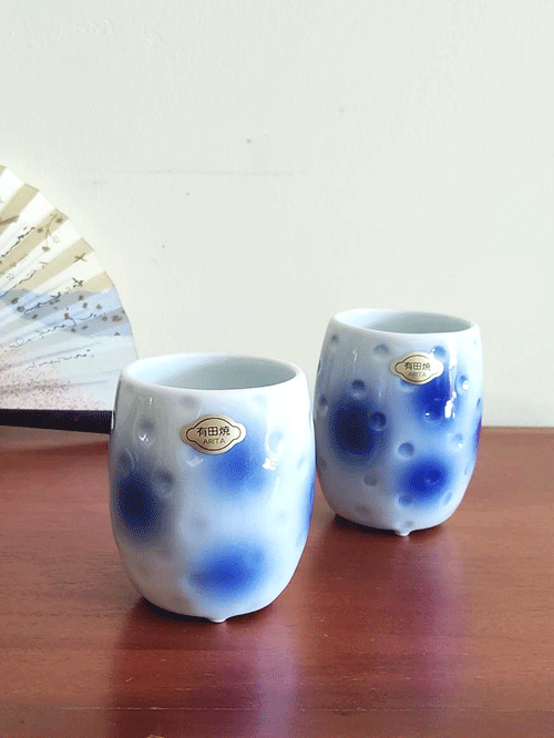 Experience the elegance of Arita ware with this exquisite Naga Yunomi (tall teacup). Aritaware , with over four centuries of rich history and tradition, is a testament to the masterful craftsmanship passed down through generations. Each piece embodies the skill and precision that Arita artisans are renowned for. This teacup features a striking blue polka dot pattern, delicately faded to create a soft, calming aesthetic. Its unique design includes three small legs at the base, adding a distinct touch of character and balance to the cup. Whether for daily use or as a display piece, this Arita ware Yunomi perfectly blends tradition and artistry. Available at j-okini.com in Malta