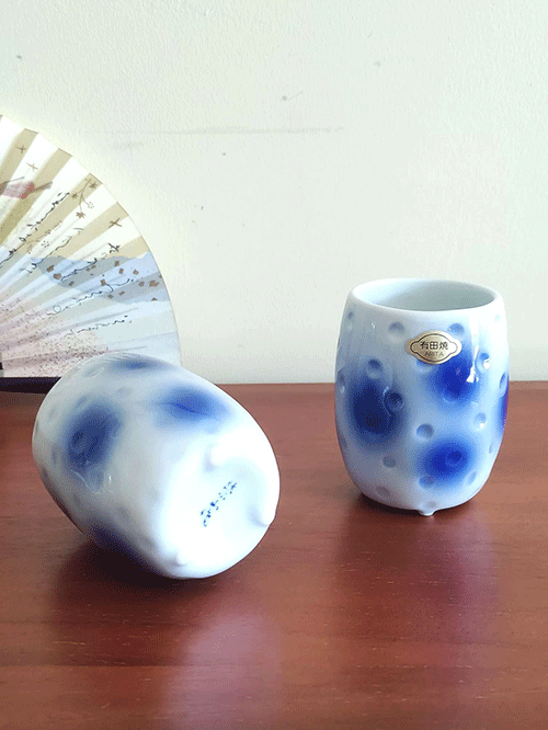 Experience the elegance of Arita ware with this exquisite Naga Yunomi (tall teacup). Aritaware , with over four centuries of rich history and tradition, is a testament to the masterful craftsmanship passed down through generations. Each piece embodies the skill and precision that Arita artisans are renowned for. This teacup features a striking blue polka dot pattern, delicately faded to create a soft, calming aesthetic. Its unique design includes three small legs at the base, adding a distinct touch of character and balance to the cup. Whether for daily use or as a display piece, this Arita ware Yunomi perfectly blends tradition and artistry.