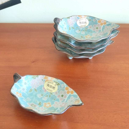 With a history dating back to the 4th century, Aritaware represents centuries of Japanese craftsmanship and tradition. Each piece reflects the skill and artistry of master craftsmen, beautifully preserved for the present. This elegant leaf-shaped porcelain plate features a delicate sakura (cherry blossom) design in light blue, making it both charming and versatile. Perfect as a soy sauce dish, for serving condiments, or even as a stylish holder for accessories on your bedroom dresser. Made in Japan, this plate embodies timeless artistry and functionality. Available at j-okini.com in Malta