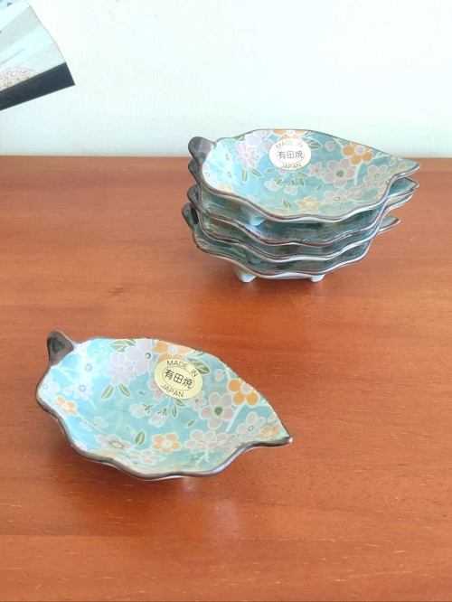 With a history dating back to the 4th century, Aritaware represents centuries of Japanese craftsmanship and tradition. Each piece reflects the skill and artistry of master craftsmen, beautifully preserved for the present. This elegant leaf-shaped porcelain plate features a delicate sakura (cherry blossom) design in light blue, making it both charming and versatile. Perfect as a soy sauce dish, for serving condiments, or even as a stylish holder for accessories on your bedroom dresser. Made in Japan, this plate embodies timeless artistry and functionality. Available at j-okini.com in Malta