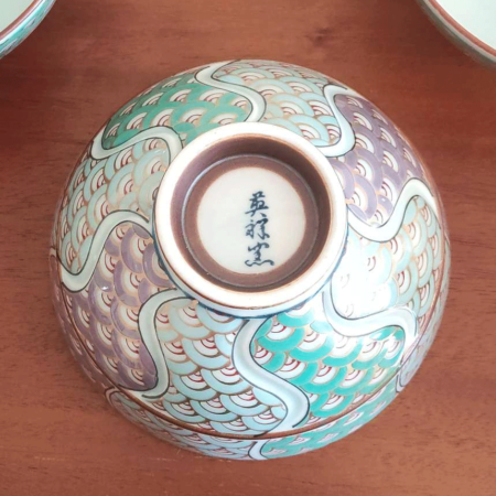 This exquisite Japanese rice bowl exemplifies the rich, over 400-year tradition of Arita ware, renowned for its timeless beauty and expert craftsmanship. Handcrafted in the famed pottery region of Arita, Japan, the bowl features a stunning 青海波 (Seigaiha) wave pattern in shades of green and purple, elegantly traced with gold accents.  The rim is adorned with intricate navy blue detailing, enhancing the bowl’s overall sophistication. Each bowl is meticulously hand-painted, showcasing the artistry and skill of the craftsmen who continue to honor Arita's proud ceramic heritage. Its versatile size makes it ideal for serving rice, soups, or even desserts, adding a refined touch to any meal. Made in Japan What is the Seigaiha Pattern? The 青海波 (Seigaiha), or "blue ocean wave" pattern, is a traditional Japanese motif symbolizing the calm and endless waves of the sea. This auspicious design is believed to represent a wish for a peaceful and prosperous life. Available at j-okini in Malta