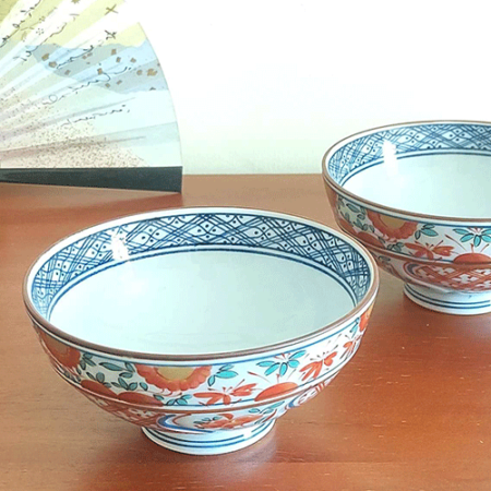 This exquisite Japanese rice bowl embodies the rich, 400-year legacy of Arita ware, celebrated for its timeless elegance and masterful craftsmanship. Handcrafted in the renowned pottery region of Arita, Japan, this bowl showcases the traditional Aka-e technique, a style known for its vibrant use of red, green, and blue hues.  The intricate design combines delicate floral motifs with geometric patterns, while the rim is beautifully accented with navy blue detailing, adding a layer of sophistication to the piece. Each bowl is meticulously hand-painted, reflecting the artistry and dedication of Arita’s skilled craftsmen, who continue to uphold this centuries-old ceramic tradition. Its versatile size makes it perfect for serving rice, soups, or desserts, bringing a refined touch of Japanese artistry to any meal.