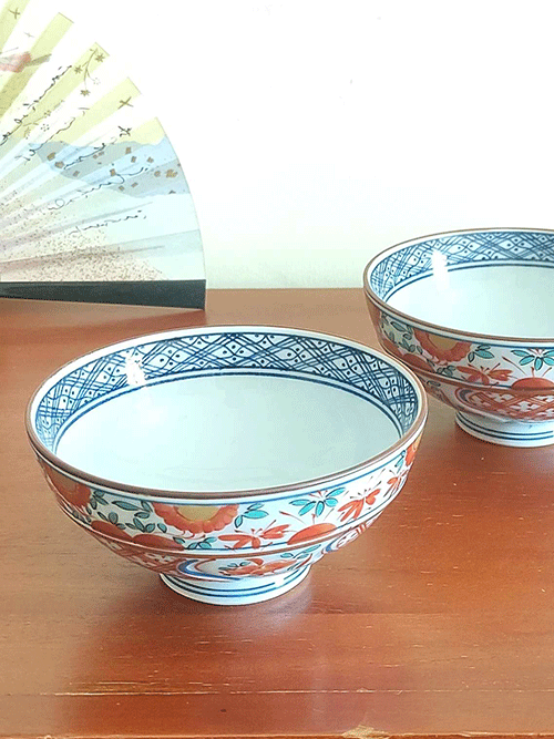 This exquisite Japanese rice bowl embodies the rich, 400-year legacy of Arita ware, celebrated for its timeless elegance and masterful craftsmanship. Handcrafted in the renowned pottery region of Arita, Japan, this bowl showcases the traditional Aka-e technique, a style known for its vibrant use of red, green, and blue hues.  The intricate design combines delicate floral motifs with geometric patterns, while the rim is beautifully accented with navy blue detailing, adding a layer of sophistication to the piece. Each bowl is meticulously hand-painted, reflecting the artistry and dedication of Arita’s skilled craftsmen, who continue to uphold this centuries-old ceramic tradition. Its versatile size makes it perfect for serving rice, soups, or desserts, bringing a refined touch of Japanese artistry to any meal.