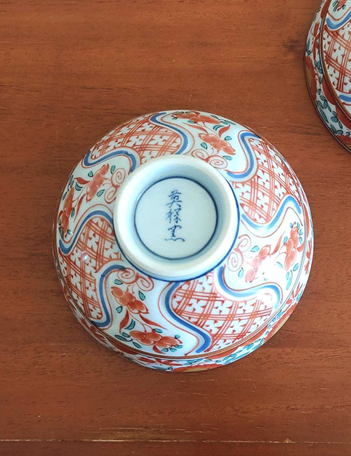 This exquisite Japanese rice bowl embodies the rich, 400-year legacy of Arita ware, celebrated for its timeless elegance and masterful craftsmanship. Handcrafted in the renowned pottery region of Arita, Japan, this bowl showcases the traditional Aka-e technique, a style known for its vibrant use of red, green, and blue hues.  The intricate design combines delicate floral motifs with geometric patterns, while the rim is beautifully accented with navy blue detailing, adding a layer of sophistication to the piece. Each bowl is meticulously hand-painted, reflecting the artistry and dedication of Arita’s skilled craftsmen, who continue to uphold this centuries-old ceramic tradition. Its versatile size makes it perfect for serving rice, soups, or desserts, bringing a refined touch of Japanese artistry to any meal.