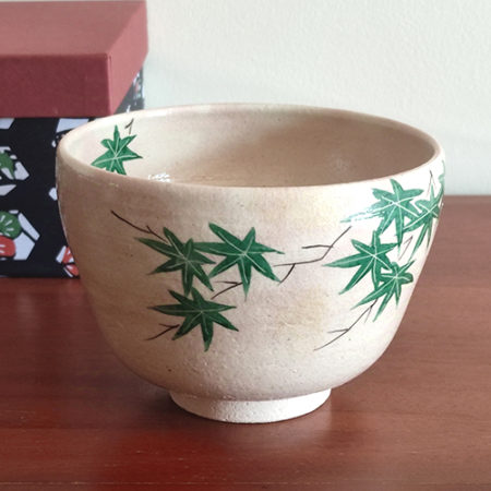 Kiyomizu-ware Matcha bowl with green maple leaves design on a warm beige background, inspired by Japanese summer landscapes. Available at j-okini.com in Malta