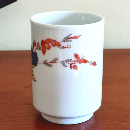 vintage teacup, crafted from white porcelain, features a  delicate hand-painted design of vibrant green, yellow, and blue leaves with a red flower gracefully extending toward the rim.. Available at j-okini.com in Malta