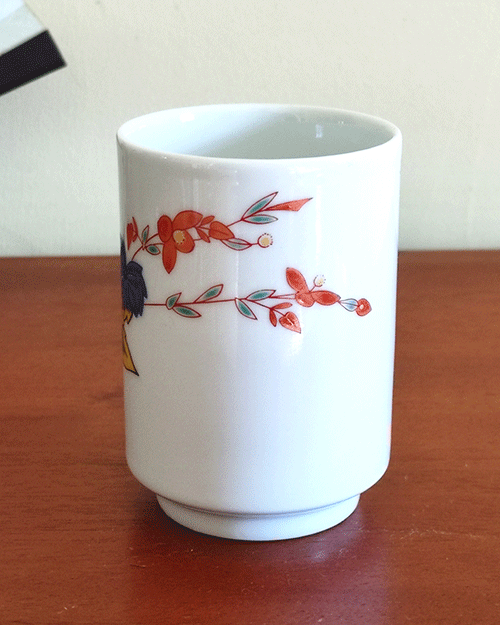 vintage teacup, crafted from white porcelain, features a  delicate hand-painted design of vibrant green, yellow, and blue leaves with a red flower gracefully extending toward the rim.. Available at j-okini.com in Malta