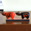 Vintage Akabeko and Kurobeko lacquered cow ornaments from Aizu, Japan, displayed on a wooden board with traditional red and black designs. The cows' heads move when pressed.