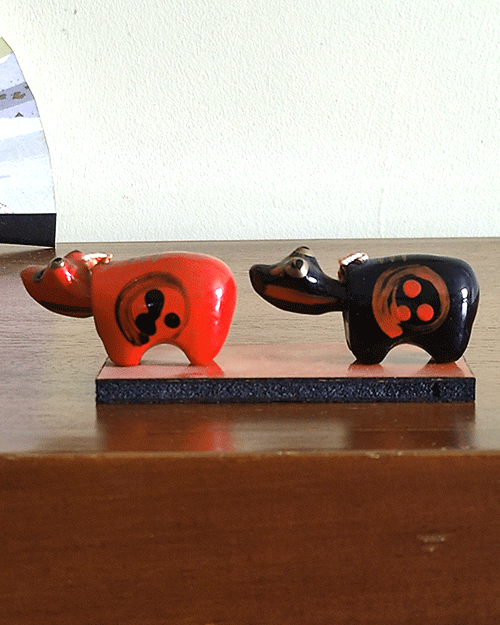 Vintage Akabeko and Kurobeko lacquered cow ornaments from Aizu, Japan, displayed on a wooden board with traditional red and black designs. The cows' heads move when pressed.