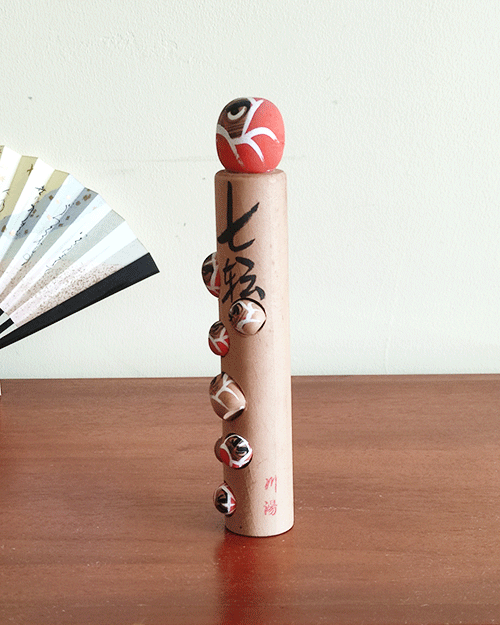 Vintage wooden Daruma doll with seven smaller Daruma figures, inscribed with the proverb 'Nanakorobi Yaoki' for resilience, stamped from Kawayu Onsen area, 17.5 cm tall with craftsman's mark. Available at j-okini.com in Malta