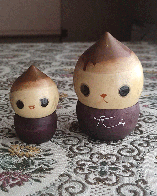 A pair of vintage wooden dolls shaped like acorns, with removable tops representing the acorn heads. The dolls show signs of age with slight scratches. One is larger, measuring approximately H10 x W6.5cm, and the smaller one is H6.5 x W4cm. These unique pieces come from a personal collection in Japan, tied to Mount Daisen in Tottori Prefecture.. Available at j-okini.com in Malta