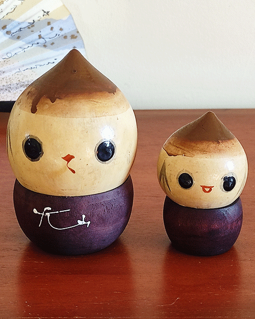 A pair of vintage wooden dolls shaped like acorns, with removable tops representing the acorn heads. The dolls show signs of age with slight scratches. One is larger, measuring approximately H10 x W6.5cm, and the smaller one is H6.5 x W4cm. These unique pieces come from a personal collection in Japan, tied to Mount Daisen in Tottori Prefecture.. Available at j-okini.com in Malta