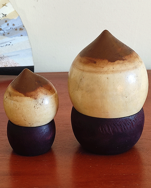 A pair of vintage wooden dolls shaped like acorns, with removable tops representing the acorn heads. The dolls show signs of age with slight scratches. One is larger, measuring approximately H10 x W6.5cm, and the smaller one is H6.5 x W4cm. These unique pieces come from a personal collection in Japan, tied to Mount Daisen in Tottori Prefecture.. Available at j-okini.com in Malta