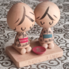 A pair of vintage wooden dolls from Izumo Taisha Shrine in Seiza position, representing a boy and girl. Hand-painted with traditional kimonos and seated with a red sake cup inscribed with "寿" (kotobuki). A faint craftsman's stamp is next to the girl on the wooden base.