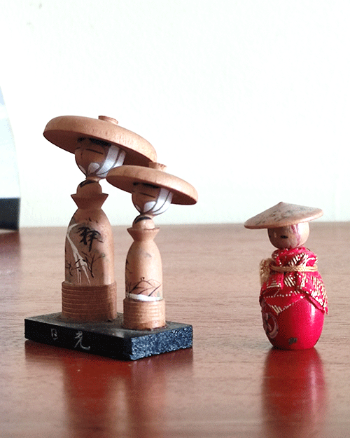 Two small vintage Japanese folk dolls from the Showa era: one in an orange kimono with a hat, and a wooden father-and-son pair standing on a wooden board with hand-painted details and traditional hats from Nikko, Tochigi Prefecture. Available at j-okini.com in Malta