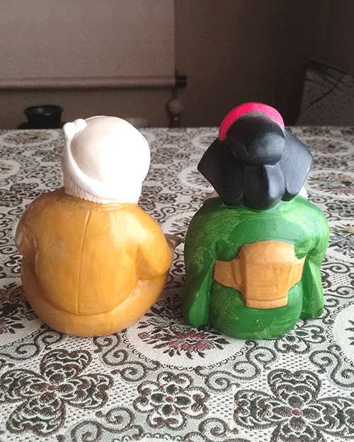 Vintage Hyottoko and Okame pottery ornaments from the Showa era, Hyottoko in a mustard kimono and Okame in a green kimono with red apron, approx. 15 cm tall, symbols of fire protection and good fortune. Available at j-okini.com in Malta