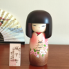 Kokeshi doll named Jokamachi featuring a beautiful depiction of a castle and delicate cherry blossoms on a soft pink kimono, symbolizing the elegance and history of Japanese heritage.. Buy it online at j-okini.com in Malta