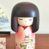 Kokeshi doll named Jokamachi featuring a beautiful depiction of a castle and delicate cherry blossoms on a soft pink kimono, symbolizing the elegance and history of Japanese heritage.. Buy it online at j-okini.com in Malta