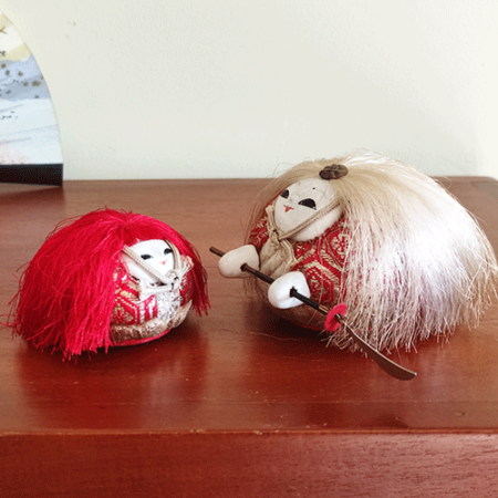 A pair of vintage Kimekomi dolls depicting a Kabuki dance. The adult doll has white hair and holds a naginata, while the child doll has red hair. Both wear detailed fabric kimonos in gold, red, and cream with hand-painted faces. Available at j-okini.com in Malta