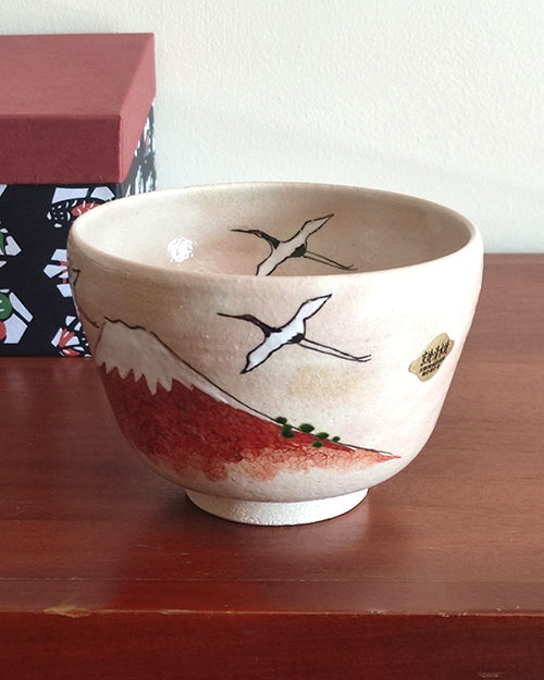 Handcrafted Kiyomizu-ware Matcha bowl featuring Red Fuji and crane design on a warm beige background with soft pink and orange speckles.. Gift idea from j-okini.com in Malta