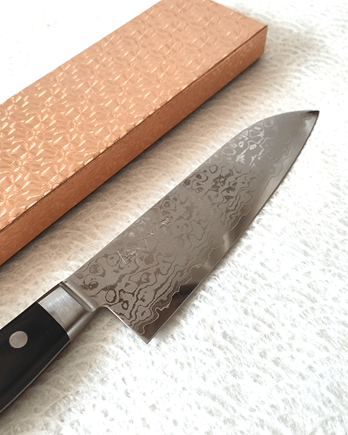 Japanese Santoku kitchen knife with a VG10 Damascus blade featuring a unique wave pattern and an elegant, simple handle. j-okini in Malta.