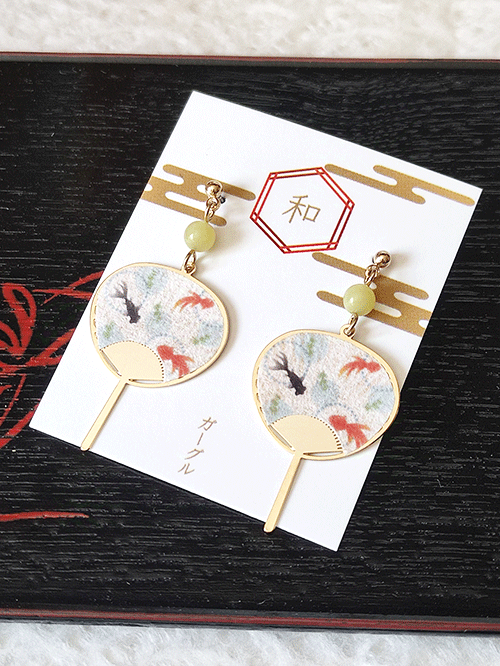 Adorable uchiwa fan-shaped earrings feature a charming design of goldfish swimming gracefully, adding a touch of seasonal elegance to your look. Perfect for a playful yet stylish accessory that evokes the spirit of Japanese summer. Available at j-okini.com in Malta