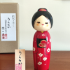 Modern Creative Kokeshi doll named Uraraka, crafted by award-winning artist Sekiguchi Toua, wearing a vibrant red kimono with plum blossom patterns, a black obi with matching design, and a plum blossom Kanzashi hair ornament in a stylish bun.. Buy it online at j-okini.com in Malta