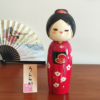 Modern Creative Kokeshi doll named Uraraka, crafted by award-winning artist Sekiguchi Toua, wearing a vibrant red kimono with plum blossom patterns, a black obi with matching design, and a plum blossom Kanzashi hair ornament in a stylish bun.. Buy it online at j-okini.com in Malta