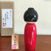 Modern Creative Kokeshi doll named Uraraka, crafted by award-winning artist Sekiguchi Toua, wearing a vibrant red kimono with plum blossom patterns, a black obi with matching design, and a plum blossom Kanzashi hair ornament in a stylish bun.. Buy it online at j-okini.com in Malta