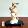 A golden dragon figurine standing 19cm tall, depicted soaring into the sky amidst white clouds, holding a "Hoju" (sacred jewel) in its claw. The dragon's dynamic pose symbolizes prosperity and improved luck, while the black lacquered base adds a touch of elegance. Gift idea from j-okini.com in Malta