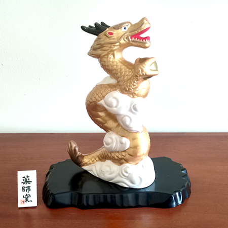 A golden dragon figurine standing 19cm tall, depicted soaring into the sky amidst white clouds, holding a "Hoju" (sacred jewel) in its claw. The dragon's dynamic pose symbolizes prosperity and improved luck, while the black lacquered base adds a touch of elegance. Gift idea from j-okini.com in Malta