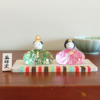 Porcelain and glass Hinamatsuri dolls, with the Emperor in green and the Empress in pink, each adorned with intricate floral designs and displayed on a wooden platform. Wedding gift. j-okini.com in Malta