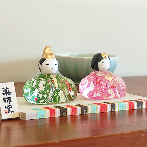 Porcelain and glass Hinamatsuri dolls, with the Emperor in green and the Empress in pink, each adorned with intricate floral designs and displayed on a wooden platform. Wedding gift. j-okini.com in Malta