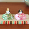 Porcelain and glass Hinamatsuri dolls, with the Emperor in green and the Empress in pink, each adorned with intricate floral designs and displayed on a wooden platform. Wedding gift. j-okini.com in Malta