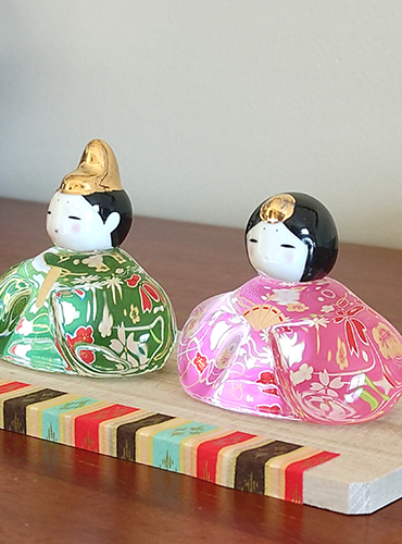 Porcelain and glass Hinamatsuri dolls, with the Emperor in green and the Empress in pink, each adorned with intricate floral designs and displayed on a wooden platform. Wedding gift. j-okini.com in Malta