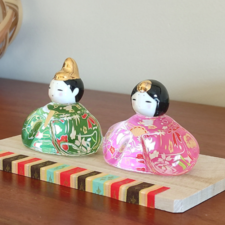 Porcelain and glass Hinamatsuri dolls, with the Emperor in green and the Empress in pink, each adorned with intricate floral designs and displayed on a wooden platform. Wedding gift. j-okini.com in Malta