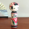 Cylindrical Creative Kokeshi doll by Miho Sasaki, featuring hand-painted chrysanthemums in red, green, and purple, with a rounded top and artist’s signature on the base. Buy online at j-okini.com in Malta