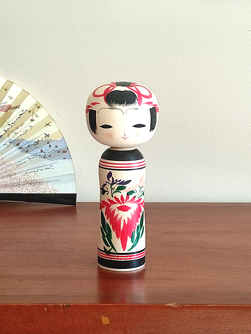 Cylindrical Creative Kokeshi doll by Miho Sasaki, featuring hand-painted chrysanthemums in red, green, and purple, with a rounded top and artist’s signature on the base. Buy online at j-okini.com in Malta