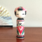 Cylindrical Creative Kokeshi doll by Miho Sasaki, featuring hand-painted chrysanthemums in red, green, and purple, with a rounded top and artist’s signature on the base. Buy online at j-okini.com in Malta